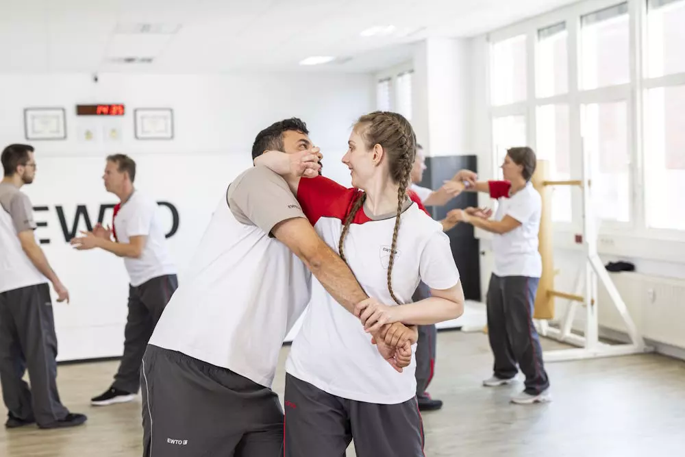 Erwachsene Frauen und Männer üben gemeinsam Wing Tsun Selbstverteidigung in hellem EWTO Trainingsraum